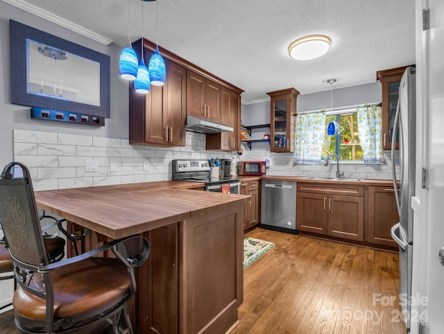 kitchen featuring sink, butcher block countertops, light wood-type flooring, appliances with stainless steel finishes, and pendant lighting