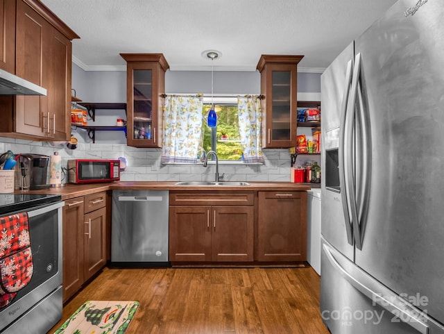 kitchen featuring sink, light wood-type flooring, ornamental molding, appliances with stainless steel finishes, and pendant lighting