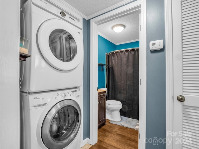 laundry area with a textured ceiling, ornamental molding, stacked washing maching and dryer, and hardwood / wood-style floors