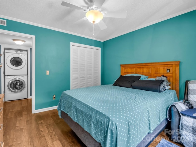 bedroom with crown molding, ceiling fan, a closet, hardwood / wood-style flooring, and stacked washing maching and dryer