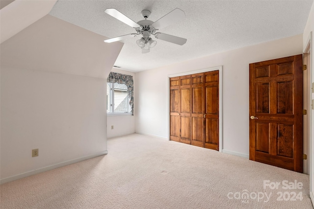 unfurnished bedroom with lofted ceiling, ceiling fan, a textured ceiling, light colored carpet, and a closet