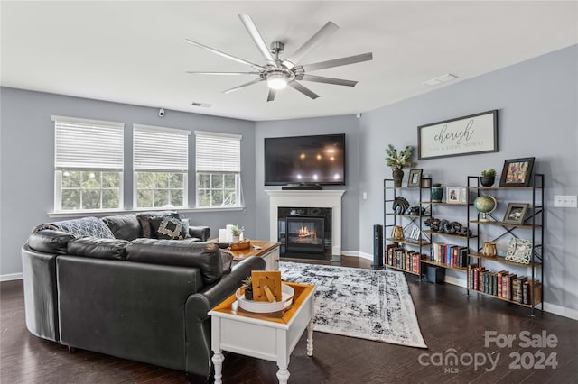 living room featuring dark wood-type flooring, a glass covered fireplace, visible vents, and baseboards