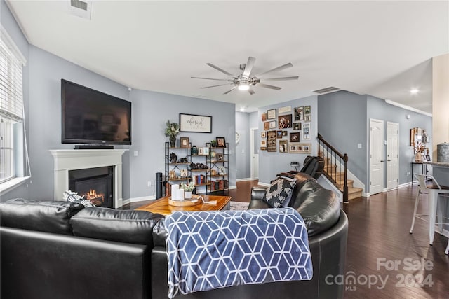 living room featuring stairs, dark wood-type flooring, a glass covered fireplace, and visible vents