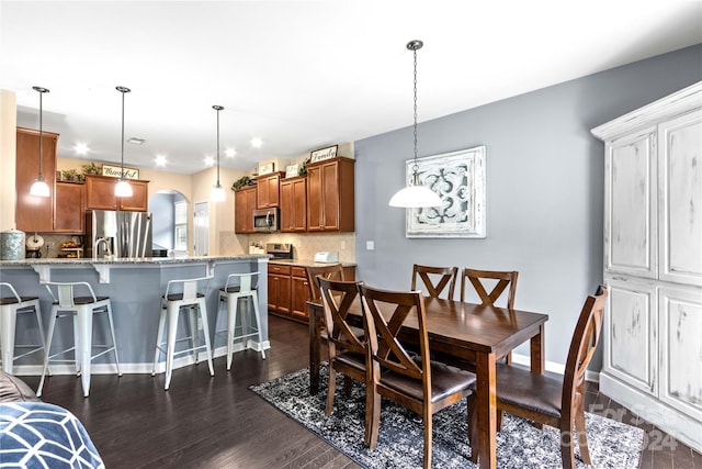 dining space featuring dark wood-style floors, baseboards, and arched walkways