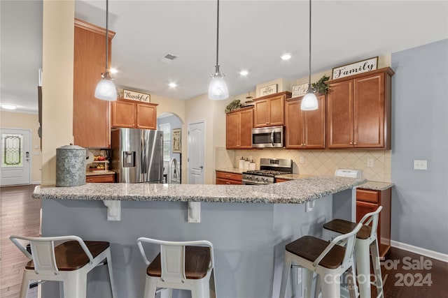 kitchen with brown cabinetry, arched walkways, stainless steel appliances, and decorative light fixtures