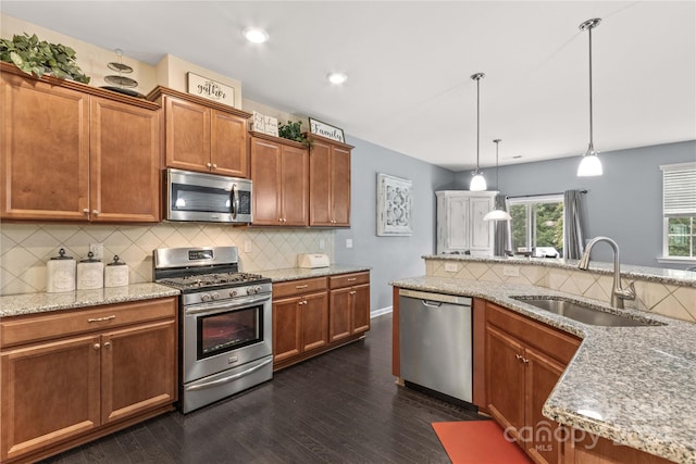 kitchen with light stone counters, a sink, appliances with stainless steel finishes, brown cabinetry, and decorative light fixtures