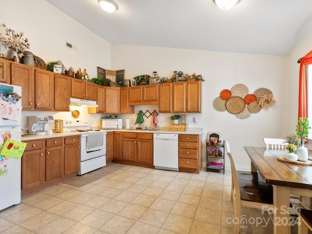 kitchen featuring brown cabinets, white appliances, light countertops, and under cabinet range hood