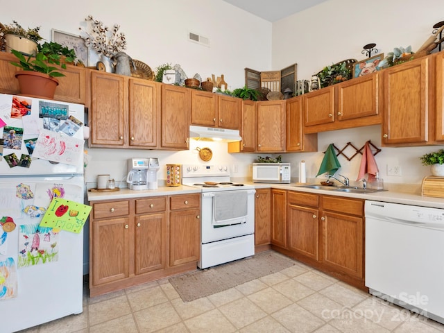 kitchen featuring under cabinet range hood, white appliances, a sink, light countertops, and brown cabinets