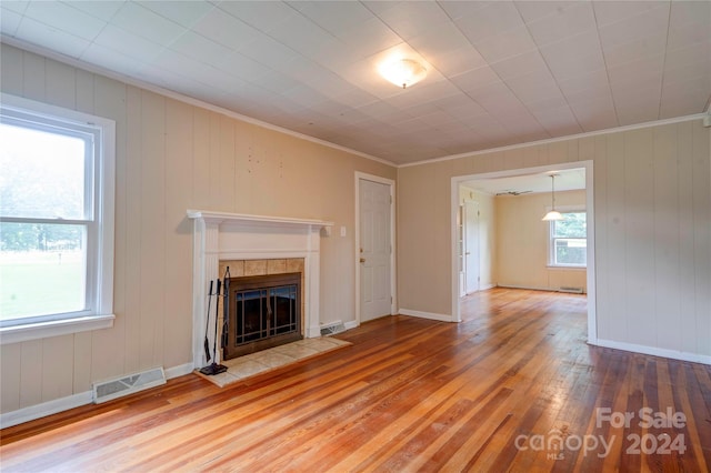 unfurnished living room with wood-type flooring, a fireplace, wood walls, and ornamental molding