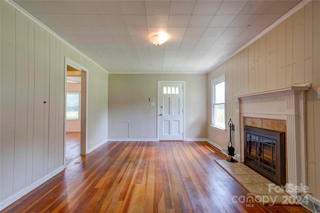 unfurnished living room with hardwood / wood-style flooring, plenty of natural light, wood walls, and a tiled fireplace