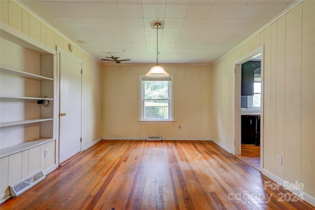 empty room featuring wooden walls, light hardwood / wood-style flooring, built in features, and ornamental molding