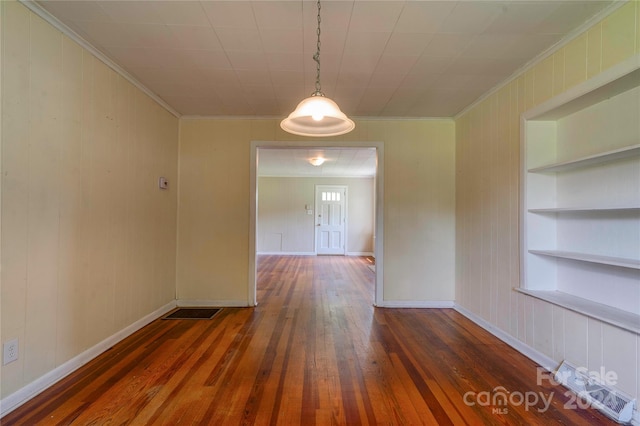 empty room with crown molding, built in shelves, and dark wood-type flooring