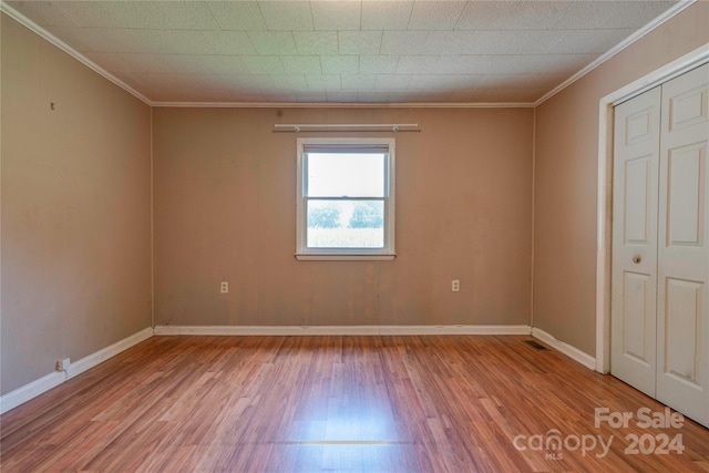 unfurnished bedroom with light wood-type flooring, a closet, and crown molding