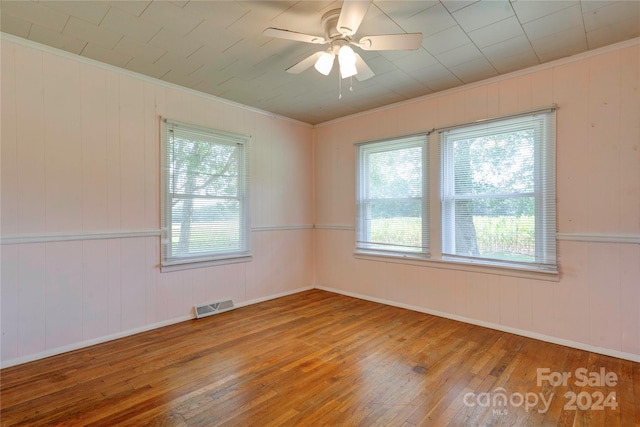 spare room with ceiling fan, hardwood / wood-style flooring, wooden walls, and crown molding