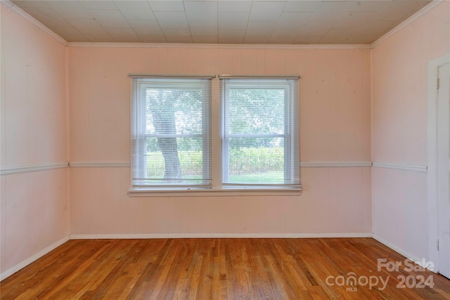 spare room featuring wood walls, hardwood / wood-style flooring, and crown molding