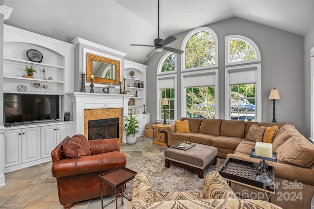 tiled living room with ceiling fan, high vaulted ceiling, built in shelves, and a tile fireplace