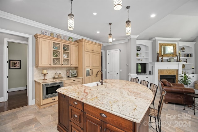 kitchen with decorative backsplash, light hardwood / wood-style flooring, stainless steel microwave, light stone countertops, and an island with sink