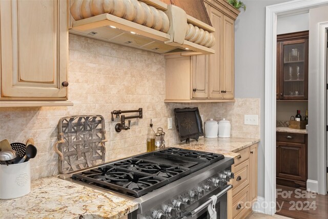 kitchen featuring tasteful backsplash, light brown cabinets, wall chimney exhaust hood, and high end stove