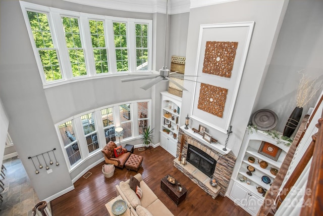 living room with a fireplace, dark hardwood / wood-style flooring, crown molding, ceiling fan, and a high ceiling