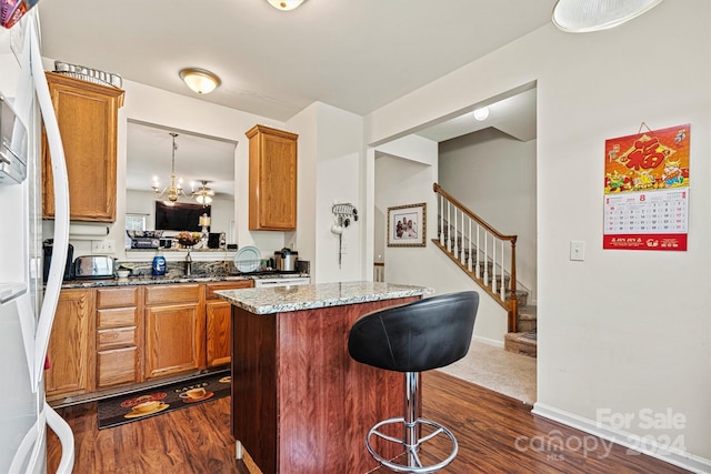 kitchen with dark stone counters, sink, a center island, dark wood-type flooring, and a breakfast bar area