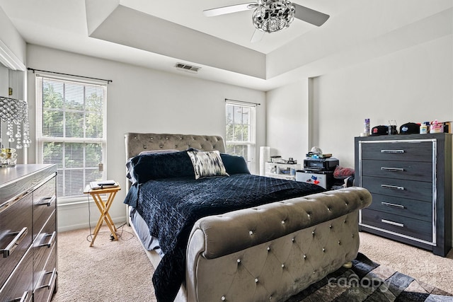 carpeted bedroom with ceiling fan and a raised ceiling