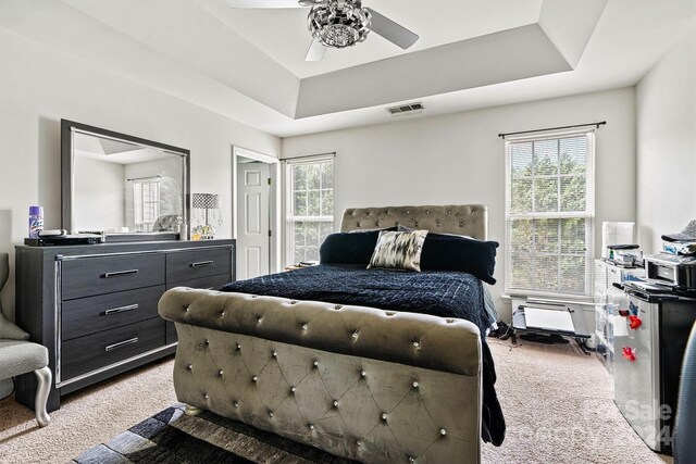 carpeted bedroom with a raised ceiling, visible vents, and a ceiling fan