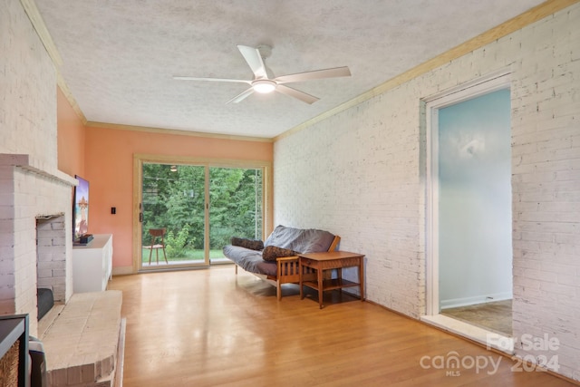 living area featuring ceiling fan, light hardwood / wood-style flooring, a brick fireplace, a textured ceiling, and crown molding