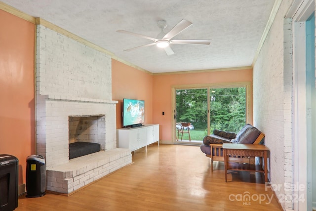 living area featuring ornamental molding, light wood-type flooring, a fireplace, a textured ceiling, and ceiling fan