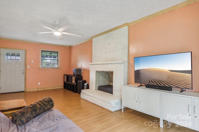 living room featuring a fireplace, ceiling fan, crown molding, and light hardwood / wood-style flooring