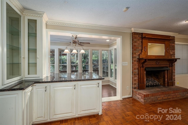 kitchen featuring a textured ceiling, a fireplace, ornamental molding, dark stone countertops, and glass insert cabinets