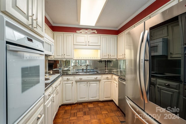 kitchen with stainless steel appliances, a sink, white cabinetry, ornamental molding, and dark stone counters