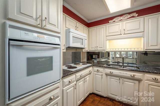 kitchen featuring dark stone countertops, ornamental molding, white appliances, sink, and white cabinets