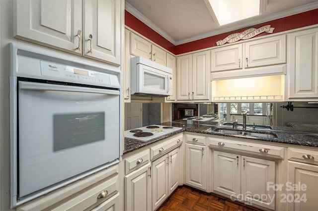 kitchen featuring white appliances, dark stone counters, crown molding, white cabinetry, and a sink