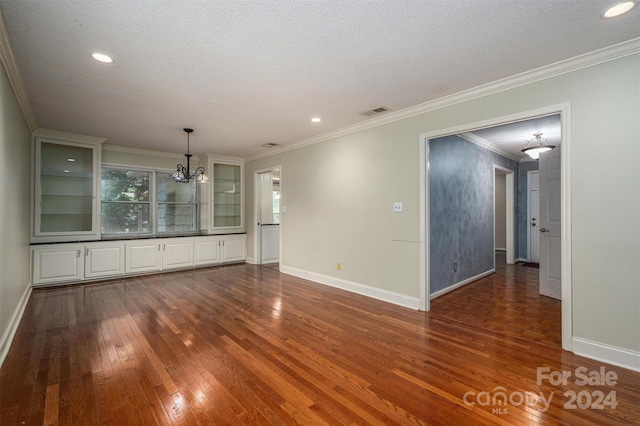 spare room featuring ornamental molding, dark wood-type flooring, a textured ceiling, and an inviting chandelier