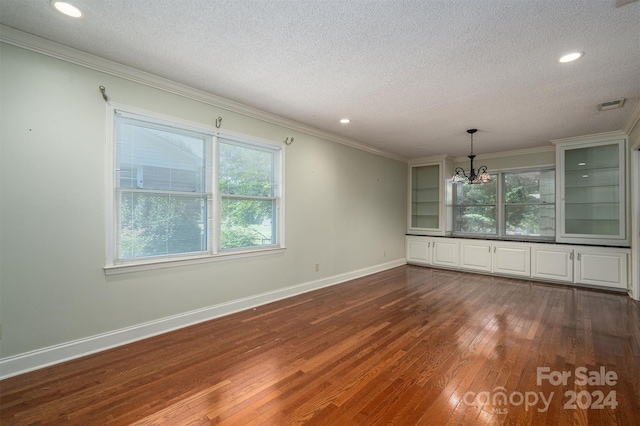 spare room with a textured ceiling, ornamental molding, a notable chandelier, and dark hardwood / wood-style flooring