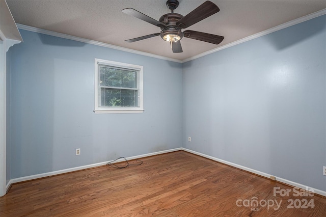 empty room with a textured ceiling, ornamental molding, wood finished floors, and baseboards