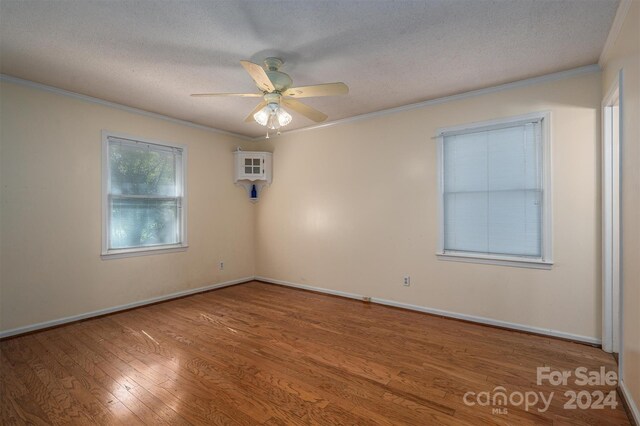 empty room with a textured ceiling, ceiling fan, ornamental molding, and wood-type flooring