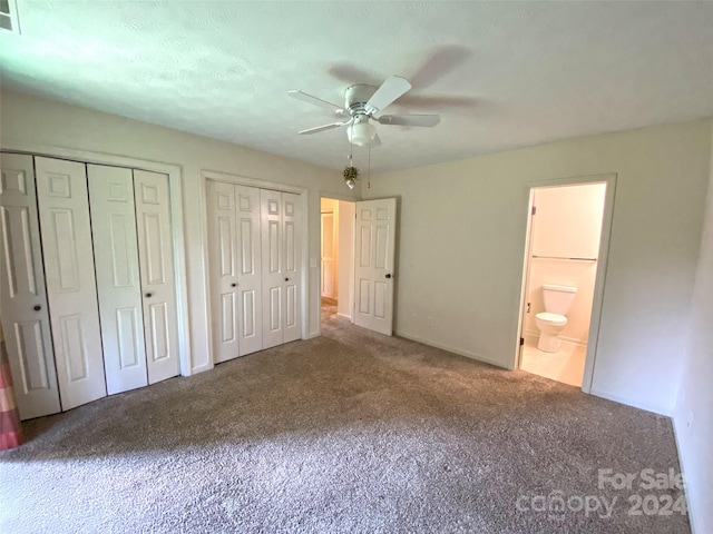 unfurnished bedroom with a textured ceiling, ensuite bath, two closets, carpet flooring, and ceiling fan