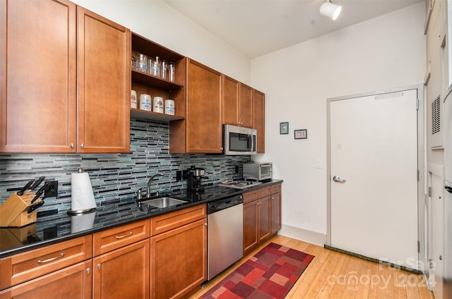 kitchen with light hardwood / wood-style flooring, dark stone countertops, backsplash, stainless steel appliances, and sink