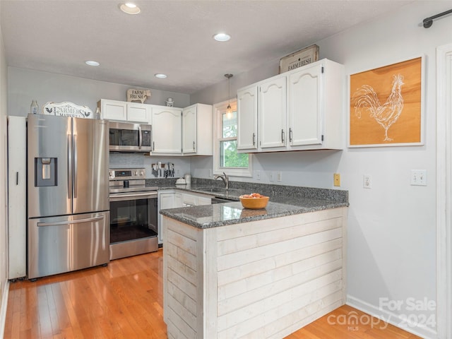 kitchen with appliances with stainless steel finishes, light hardwood / wood-style flooring, white cabinetry, and kitchen peninsula