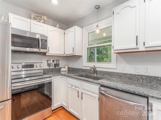 kitchen with white cabinets, light hardwood / wood-style floors, sink, dark stone countertops, and stainless steel appliances