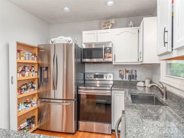 kitchen featuring light wood-type flooring, dark stone counters, white cabinetry, sink, and stainless steel appliances