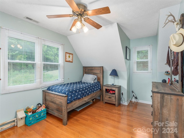 bedroom with ceiling fan, vaulted ceiling, a textured ceiling, and wood-type flooring