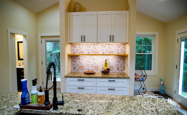 kitchen with white cabinetry, backsplash, light stone countertops, and lofted ceiling