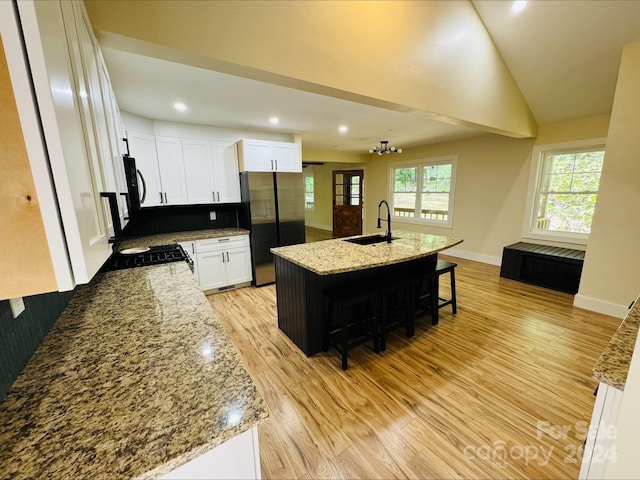 kitchen with sink, stainless steel fridge, a kitchen island with sink, light stone counters, and white cabinets