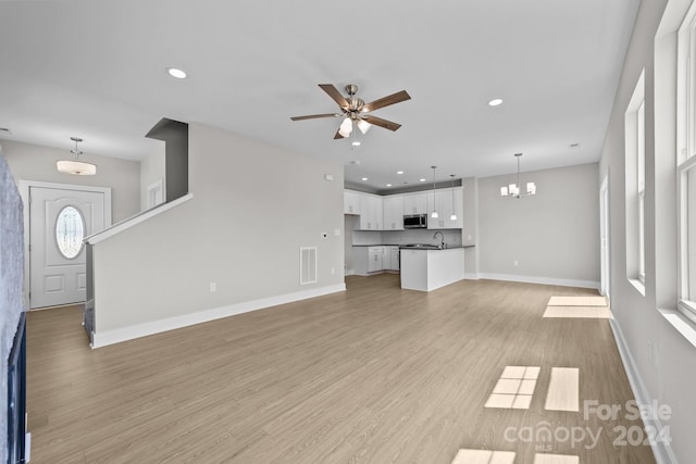 unfurnished living room featuring ceiling fan with notable chandelier, sink, and light hardwood / wood-style flooring