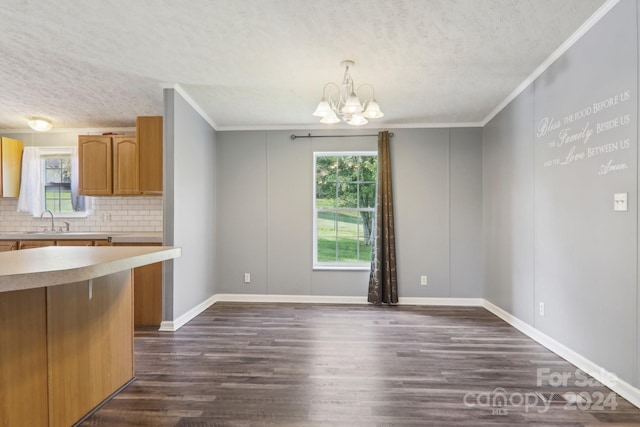 unfurnished dining area with sink, a notable chandelier, ornamental molding, and dark hardwood / wood-style floors