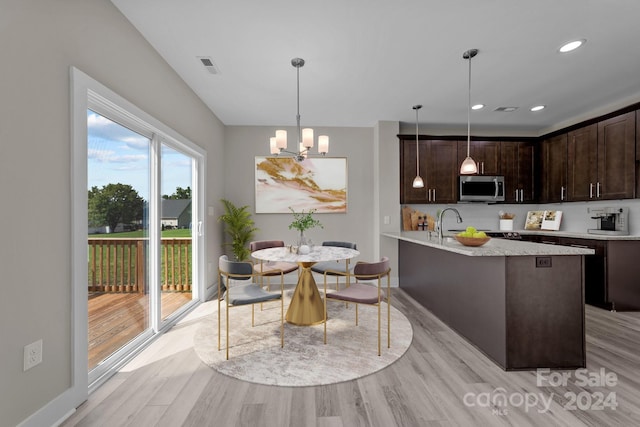 kitchen featuring light hardwood / wood-style flooring, dark brown cabinets, an island with sink, a notable chandelier, and hanging light fixtures