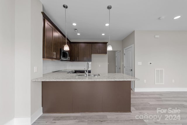 kitchen featuring sink, light hardwood / wood-style flooring, light stone counters, kitchen peninsula, and pendant lighting