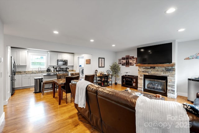 living room featuring a stone fireplace, light wood-type flooring, washer / dryer, and recessed lighting